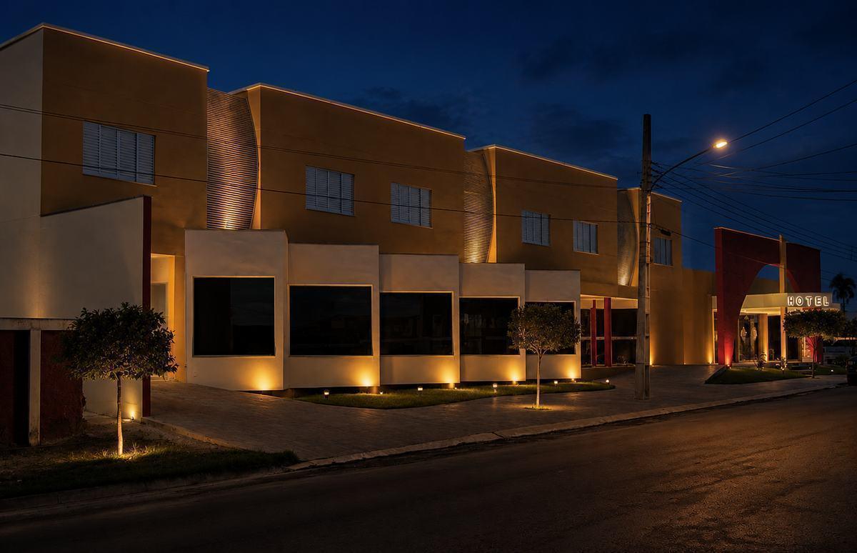 Fachada iluminada do Hotel Flor da Mata ao anoitecer, com arquitetura moderna em tons de areia e vermelho, em Guarantã do Norte