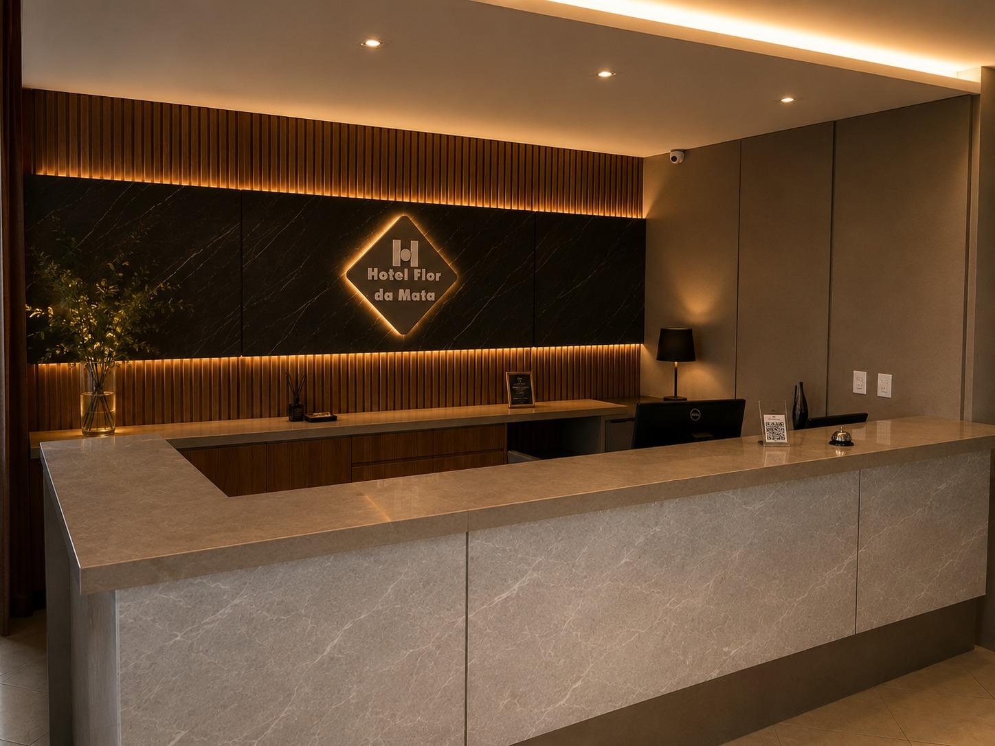 Balcão da recepção do Hotel Flor da Mata em mármore claro, com painel escuro iluminado e logotipo do hotel